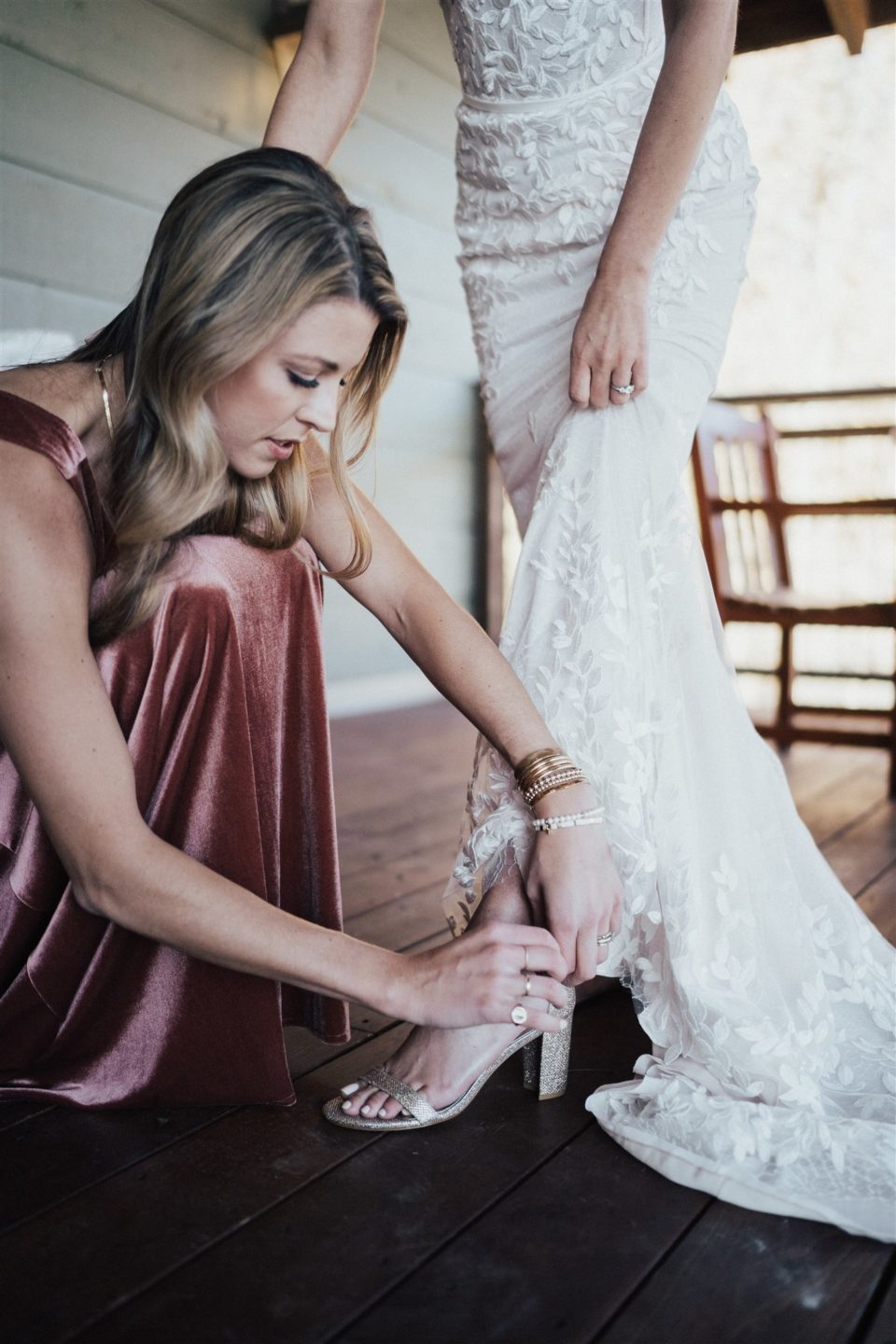 bridesmaid helps bride into shoes